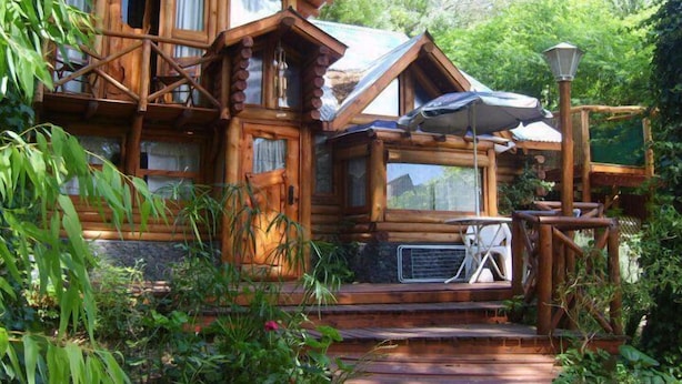 A rustic wooden cabin with a porch and a table with chairs. - Cabañas Manamar (Villa Gesell)