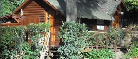 Una cabaña de madera rústica con un tejado empinado, una escalera de madera que lleva a la entrada y una ventana pequeña.