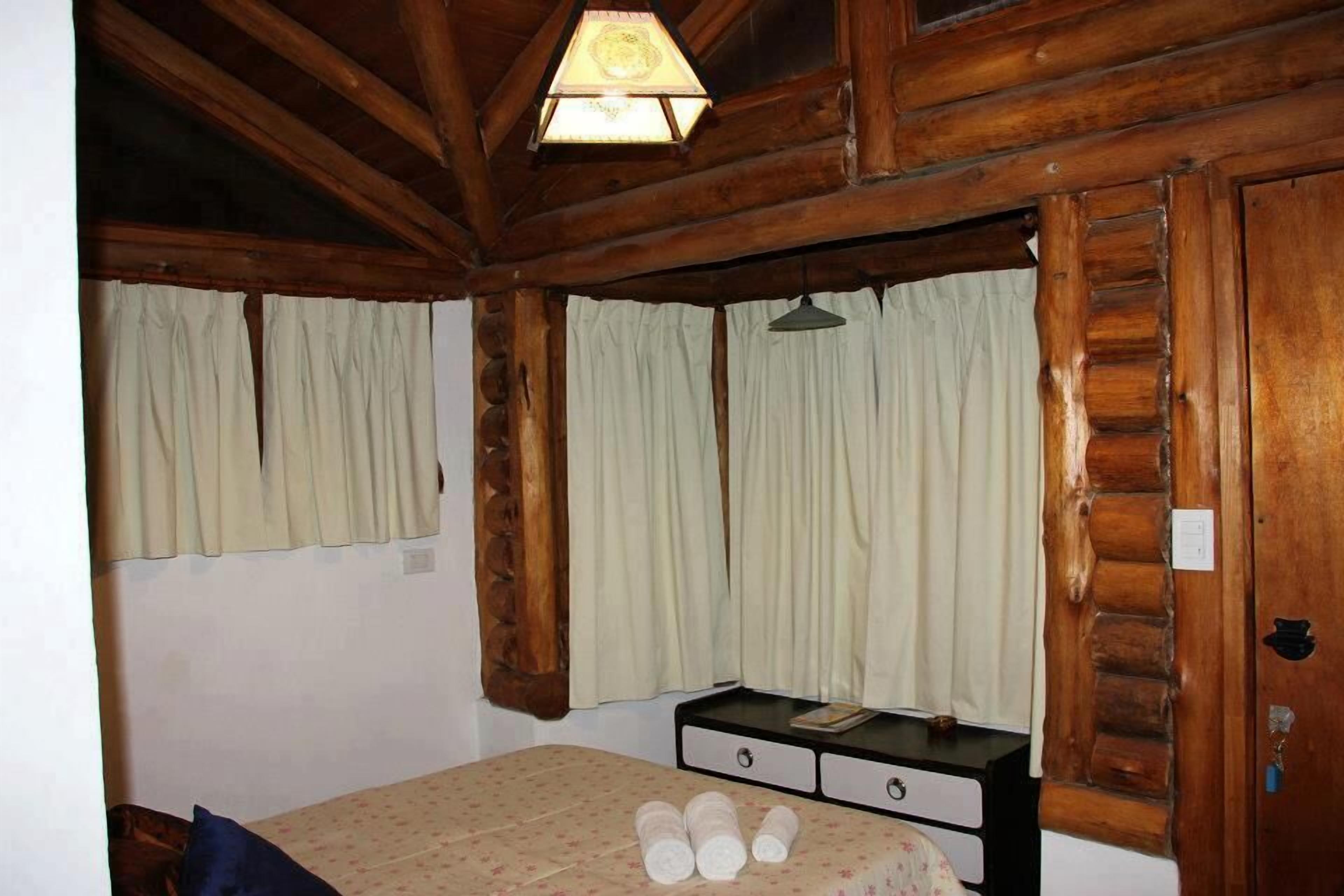 A wooden cabin room with a bed, a nightstand, and a window with curtains.