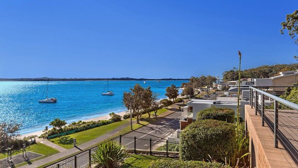 A coastal residential area with a clear view of the sea, a paved walkway, and a fenced garden area. - Kiah 8, 53 Victoria Parade - Stunning water views, Wifi & Air Con (Nelson Bay)