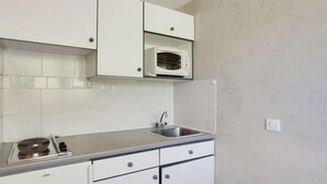 Una cocina pequeña con armarios blancos, un microondas, un fregadero y una estufa.