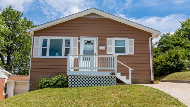 Ein eingeschossiges Haus mit Veranda, Garage und gepflegtem Rasen.