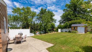 Ein Garten mit Terrasse, Grill und kleiner Gartenhütte.