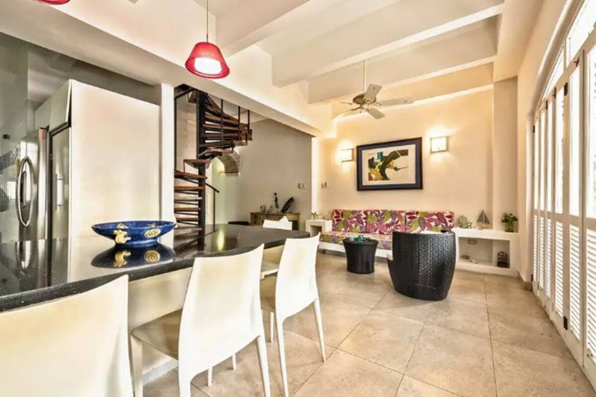 Una cocina moderna con comedor, que incluye una encimera negra, sillas blancas y una olla grande de color negro.