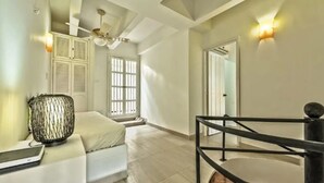 A modern bedroom with a bed, a bedside table, a lamp, a ceiling fan, and a staircase. - Santo Domingo Condos by Velvet Luxury (Cartagena)