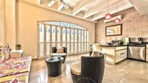 A modern living room with a sofa, two round wicker chairs, a coffee table, and a kitchen area with a brick wall, a sink, and a stove. - Santo Domingo Condos by Velvet Luxury (Cartagena)