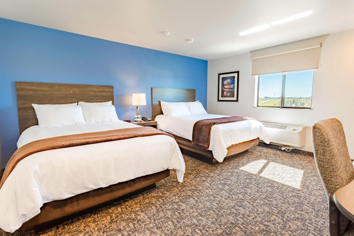 A hotel room with two beds, a desk, a chair, a window with a view, and a radiator.
