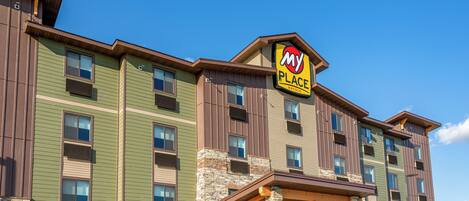 A multi-story hotel with a 'My Place' sign, featuring a mix of green and brown exterior walls, stone accents, and a covered outdoor area.