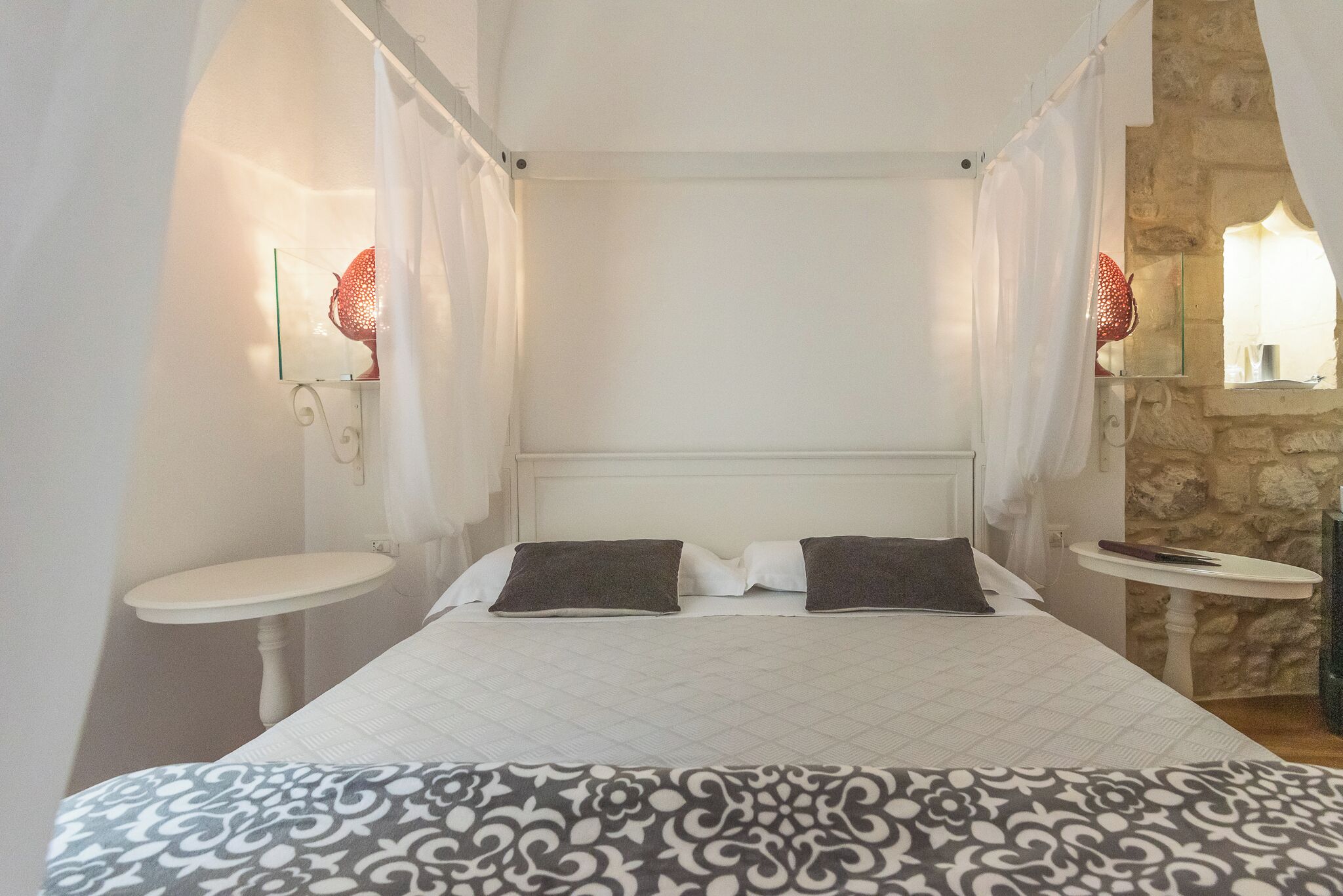 A hotel room with a bed, two bedside tables, a small round table, and a stone wall.