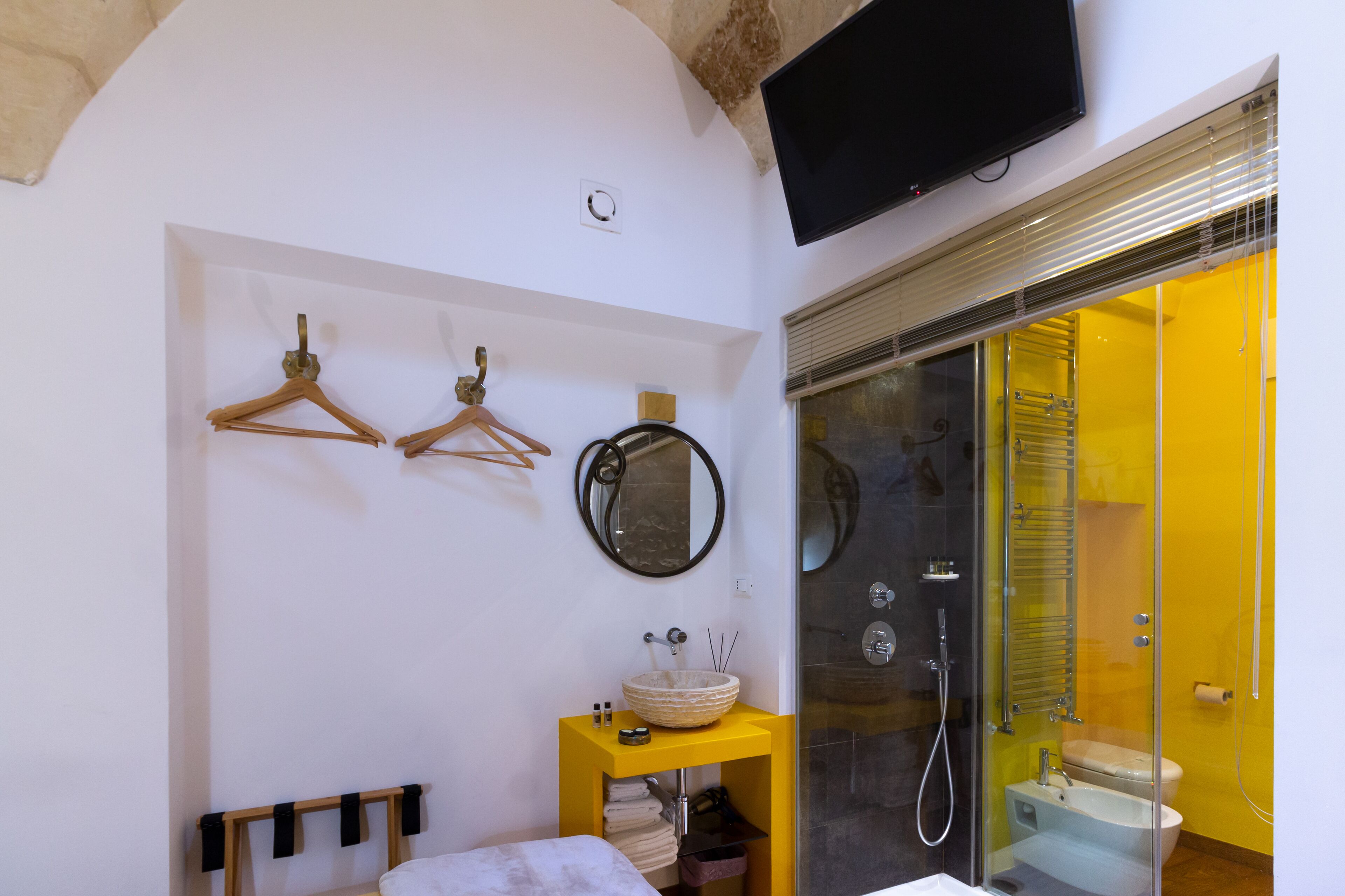 Un baño con una pared amarilla, cerramiento de ducha de vidrio, un lavabo blanco y un espejo.