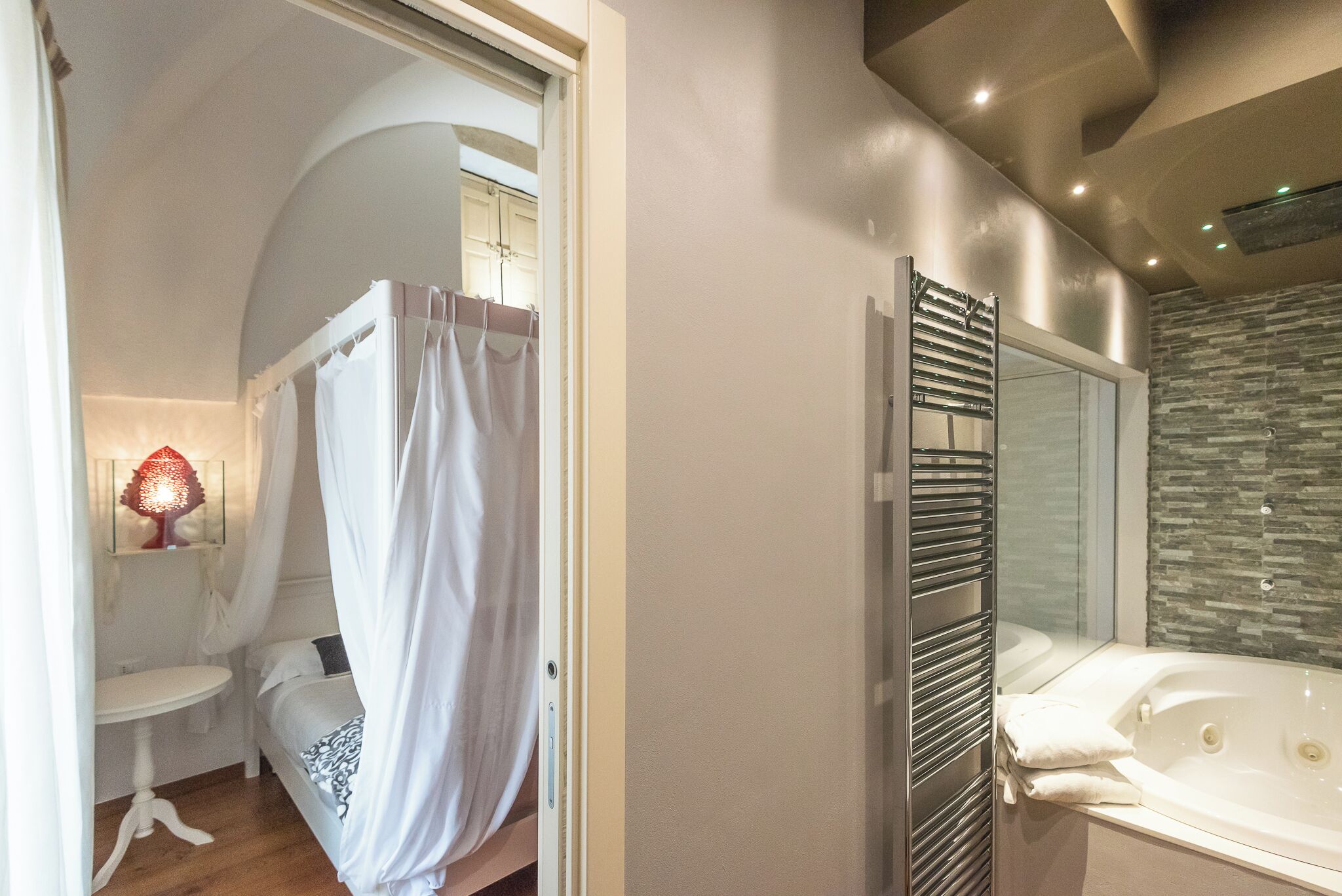 A bedroom with a bed, bedside table, and a bathroom with a bathtub and shower.