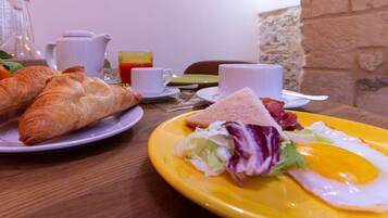 A breakfast table with croissants, a sandwich, a fried egg, and a glass of juice.