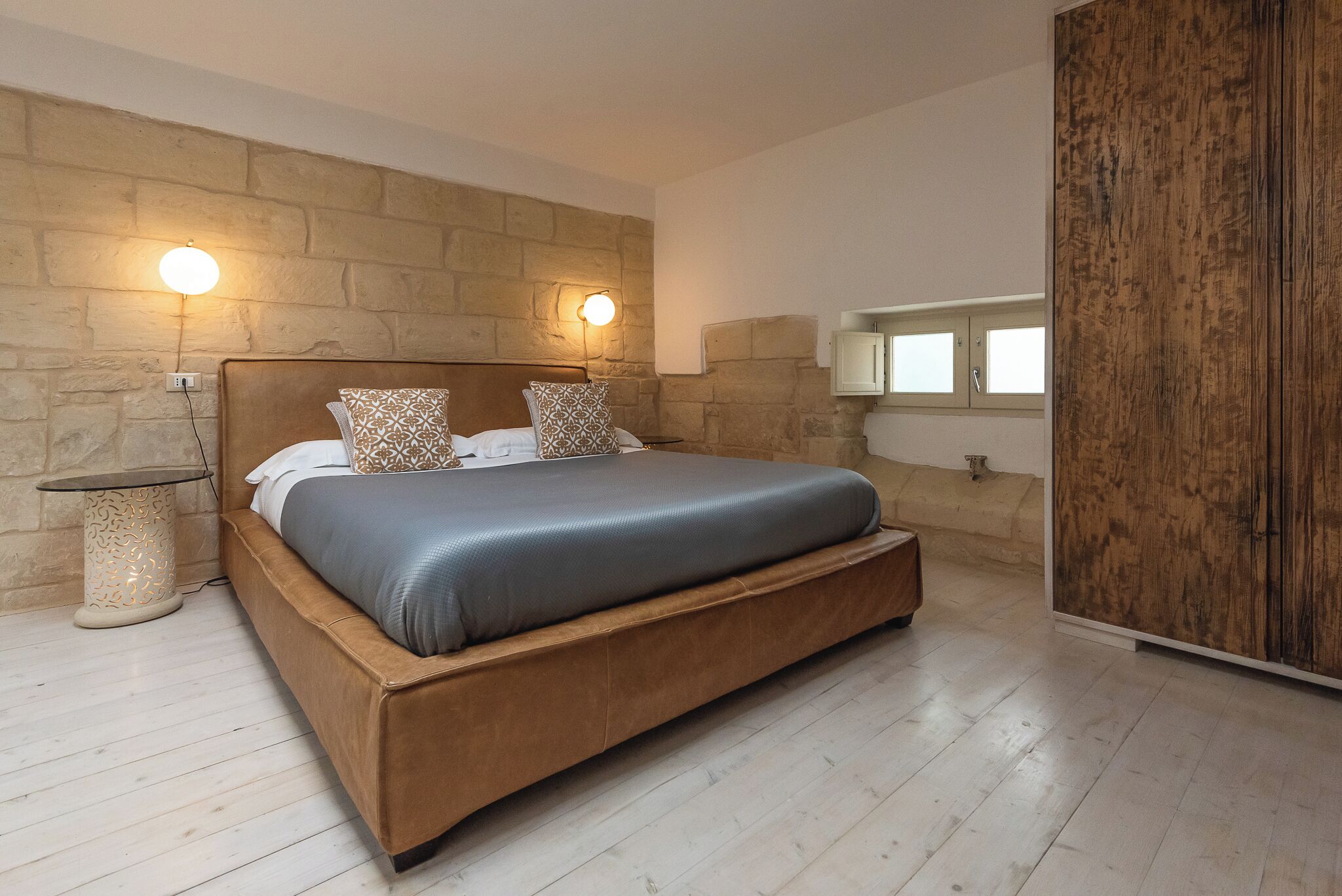 Ein Schlafzimmer mit einem großen Bett, einer Steinwand und einem Holzschrank.