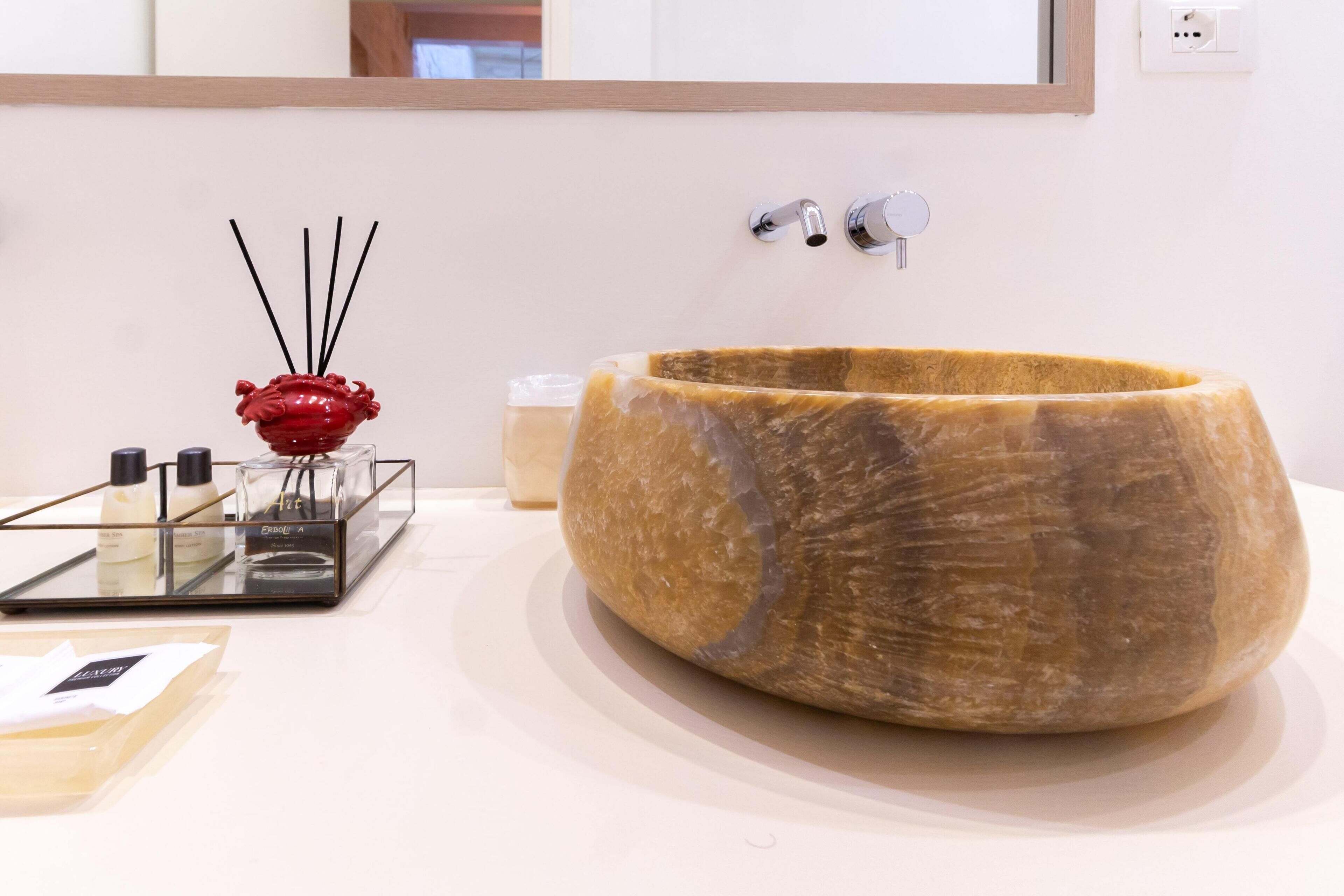 A bathroom with a large, oval-shaped stone sink, a red decorative vase, and a glass tray with toiletries.