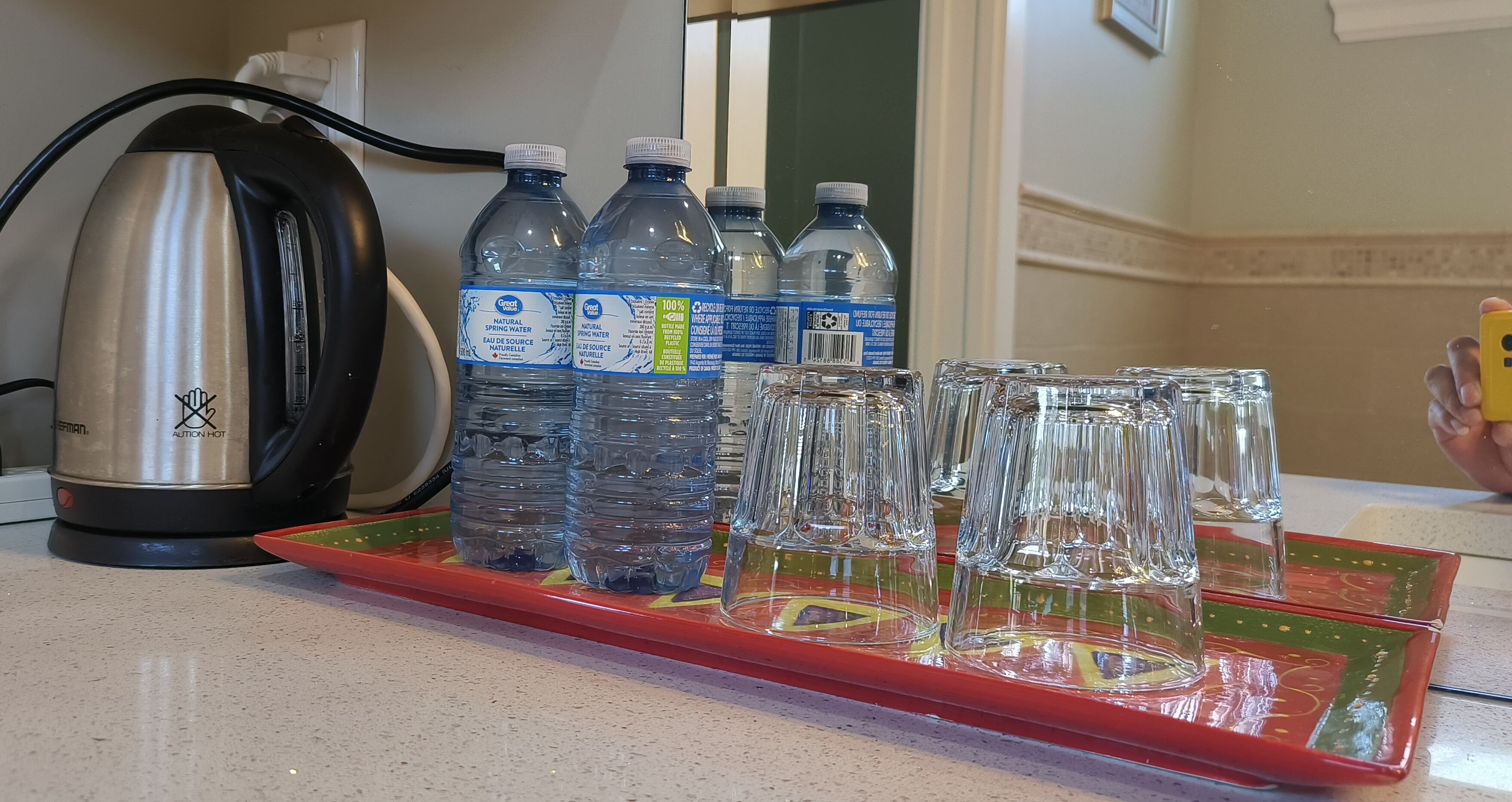 A kitchen counter with a kettle, water bottles, and glasses on a tray.
