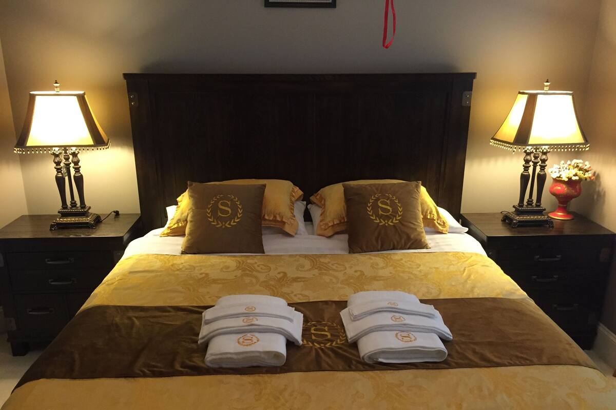 Ein Hotelzimmer mit einem großen Bett, zwei Nachttischen, zwei Lampen und einer Vase mit Blumen.