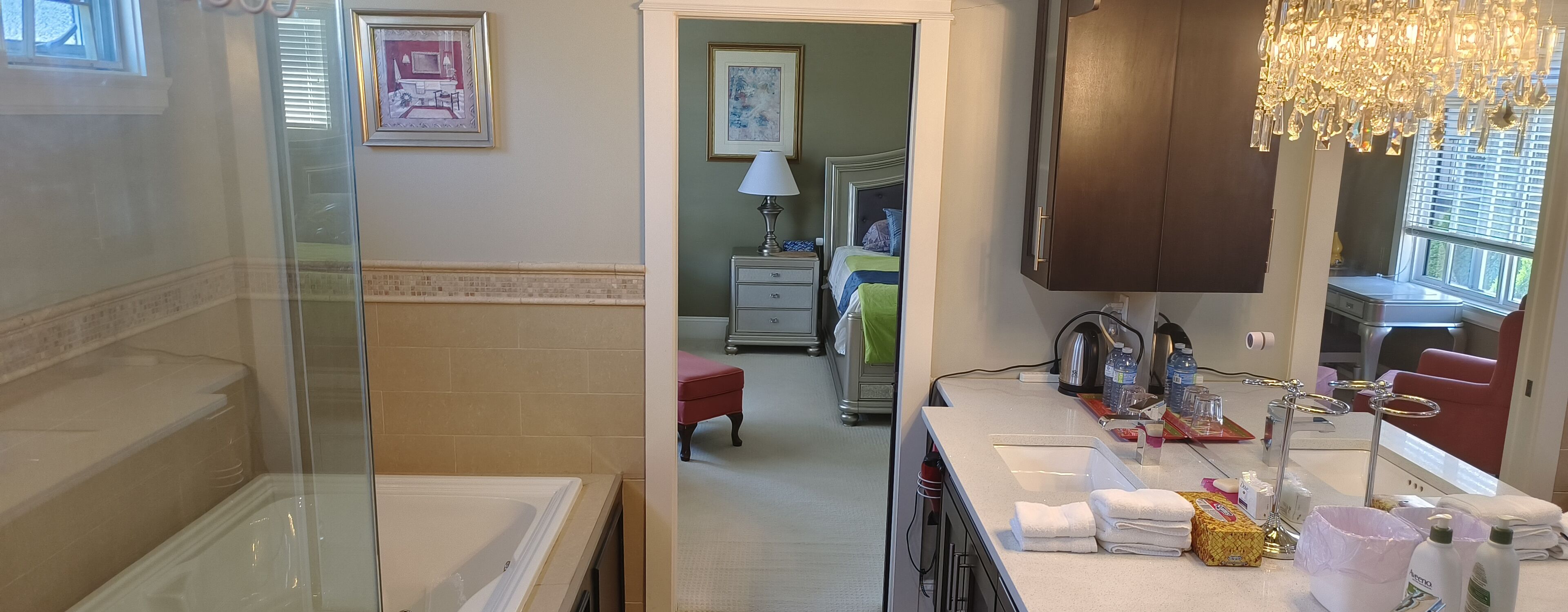 Un baño de hotel con una bañera, un lavabo y una zona de tocador. Hay un banco rojo y un espejo sobre el lavabo.