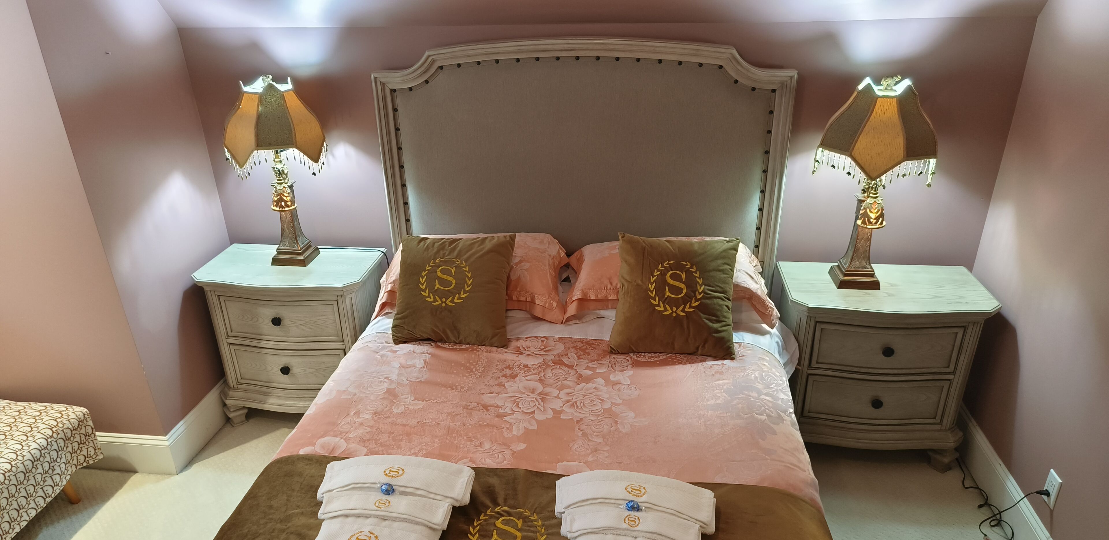 A neatly arranged bedroom with a large bed, two bedside tables with lamps, and a small bedside table with a lamp.