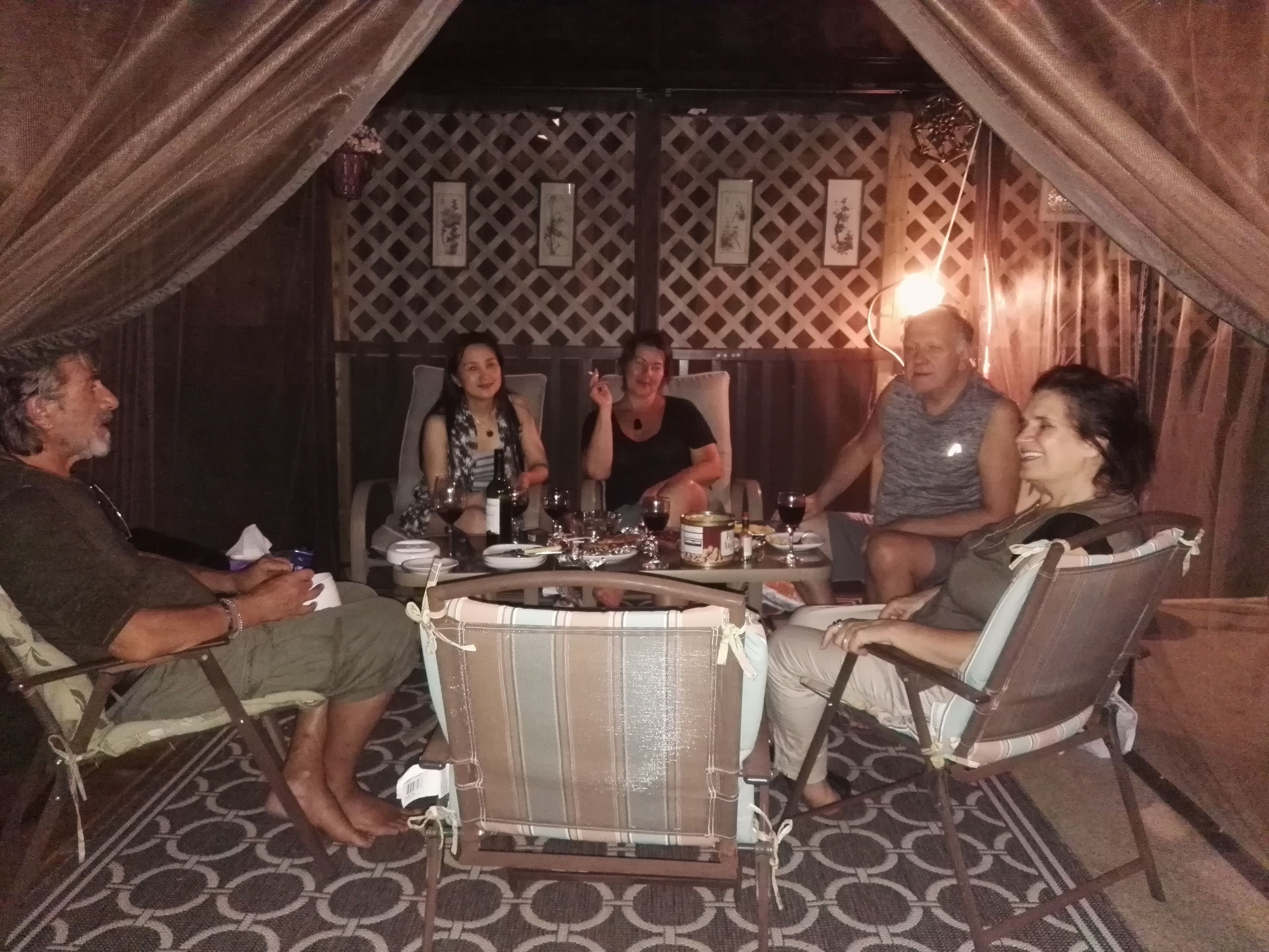 A group of people seated around a table with drinks and food, in a room with patterned flooring and curtains.