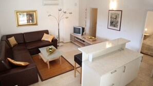 A modern living room with a brown sofa, a coffee table, a TV, and a kitchen area with a white countertop.