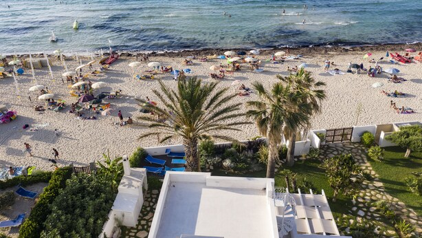 Ein Strand mit Liegestühlen, Sonnenschirmen und Palmen.