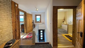 A spacious hallway with a wooden staircase, a small window, and a bathroom visible in the background.