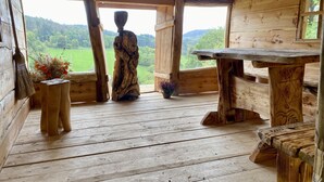 A rustic wooden cabin with a large window, a wooden statue, and a table.