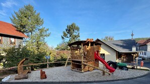 A playground with a wooden play structure, a red slide, and a green toy car.