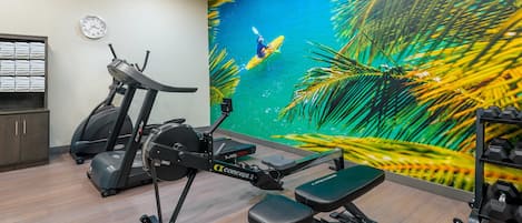 Un gimnasio con máquinas de cardio, una máquina de remo y una banca.