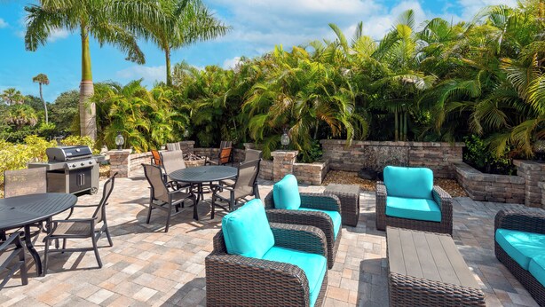An outdoor patio with wicker furniture, a grill, and lush tropical plants. - Coral Pointe Sarasota, an Ascend Collection Hotel (Sarasota)