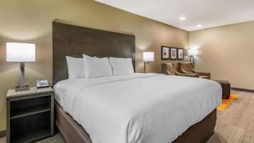 A hotel room with a large bed, a nightstand with a lamp, a chair, and a small table.