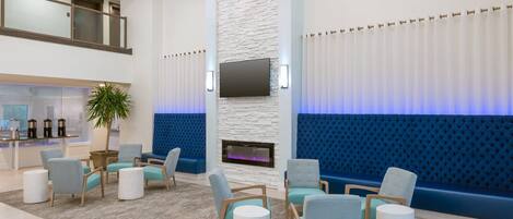A modern lobby with seating areas, a fireplace, and a television.