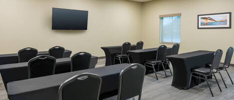 A conference room with tables and chairs, a flat-screen TV, a window with a view, and a framed picture on the wall.