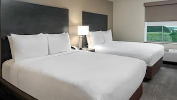 Een hotelkamer met twee bedden, een nachtkastje met lamp, een raam met uitzicht en een wandgemonteerde airconditioning.