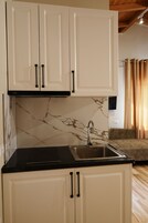 A kitchen with white cabinets, a black countertop, and a marble backsplash.