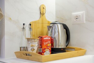 Una bandeja con una cafetera, una caja de café Lavazza Surname, un tarro de cristal y una botella de agua sobre una encimera de cocina.