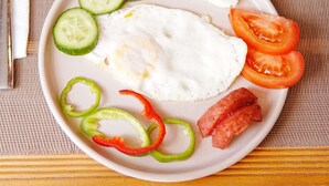A plate with an egg, cucumber slices, tomato, and bell pepper on a table.