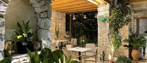 Patio esterno con pareti in pietra, travi in legno al soffitto e piante in vaso.