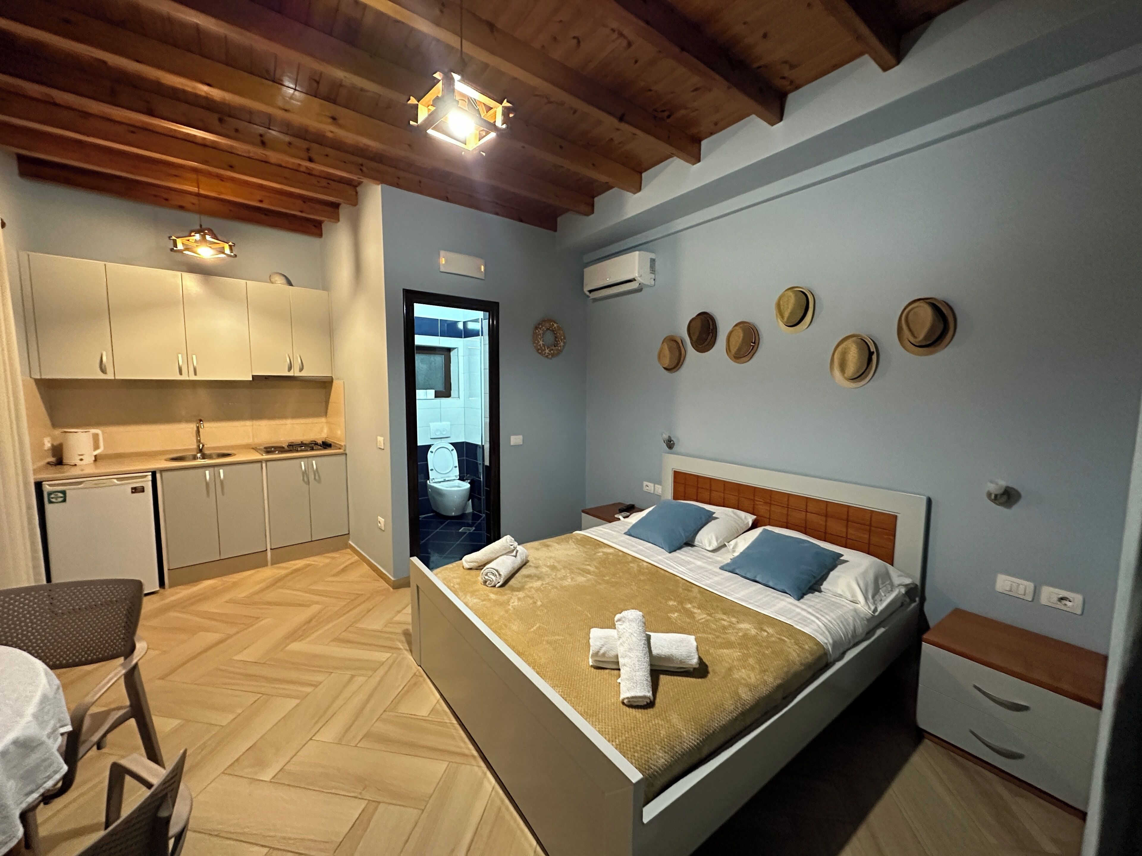 A compact hotel room with a bed, bedside tables, a small kitchenette, and a bathroom visible through an open door.