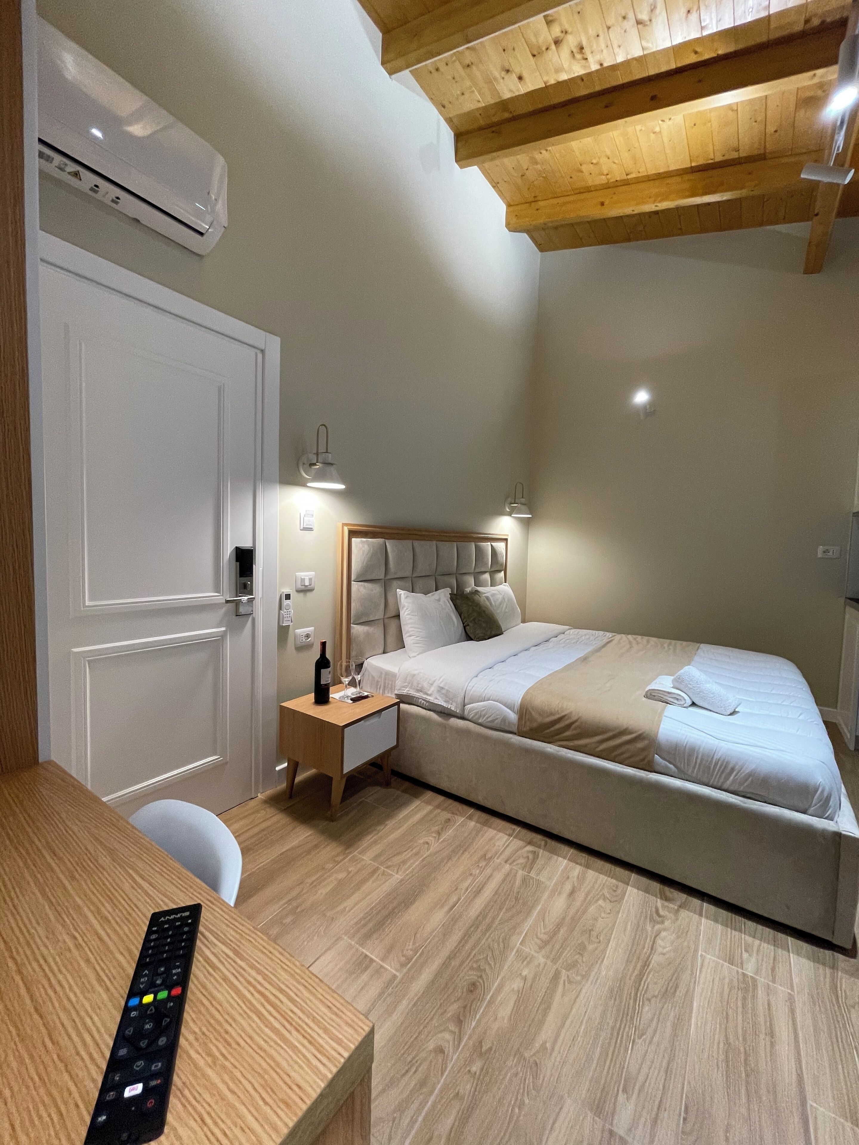 A bedroom with a bed, bedside tables, a desk, and a remote control.
