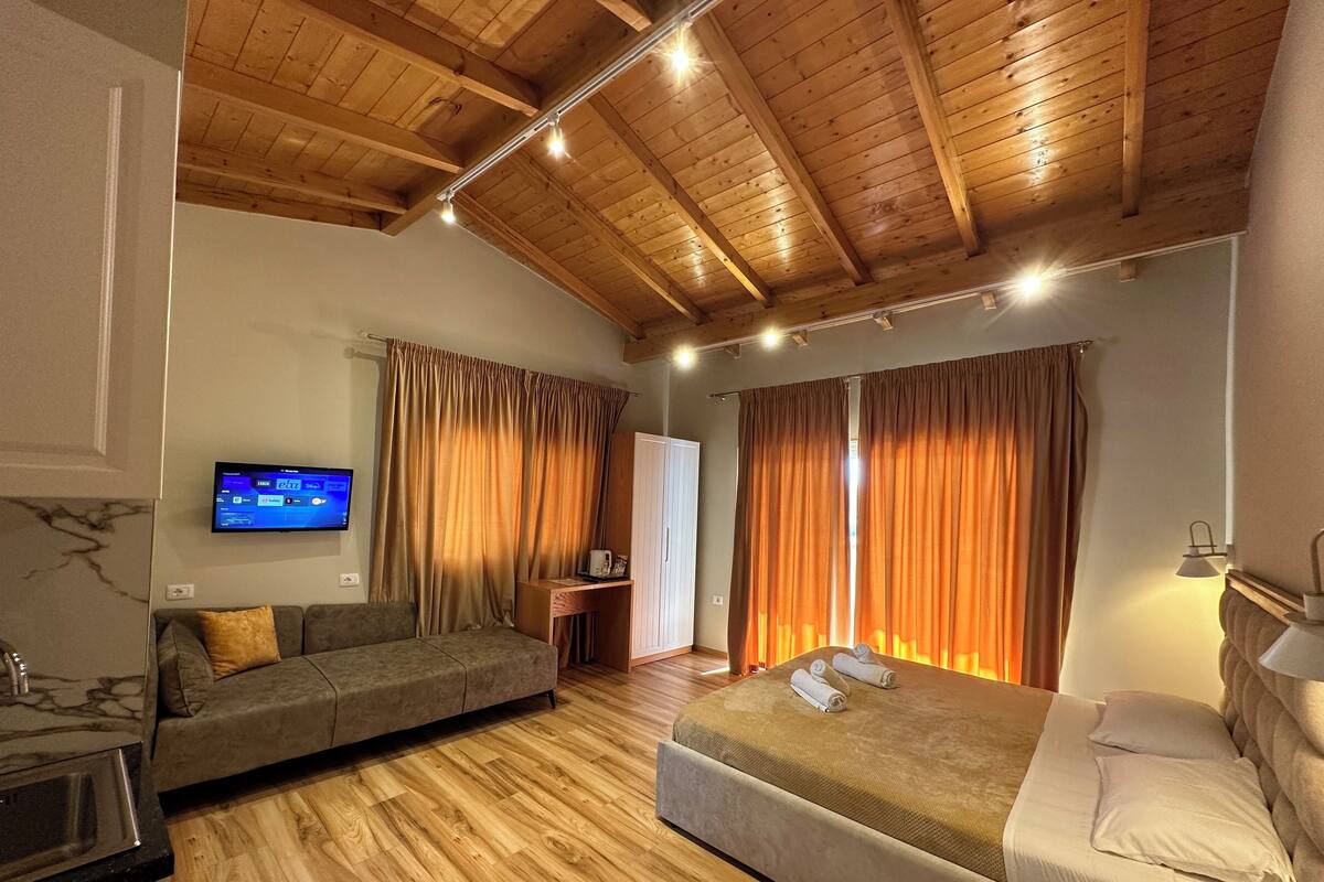 A bedroom with a wooden ceiling, a bed, a sofa, a TV, and curtains.