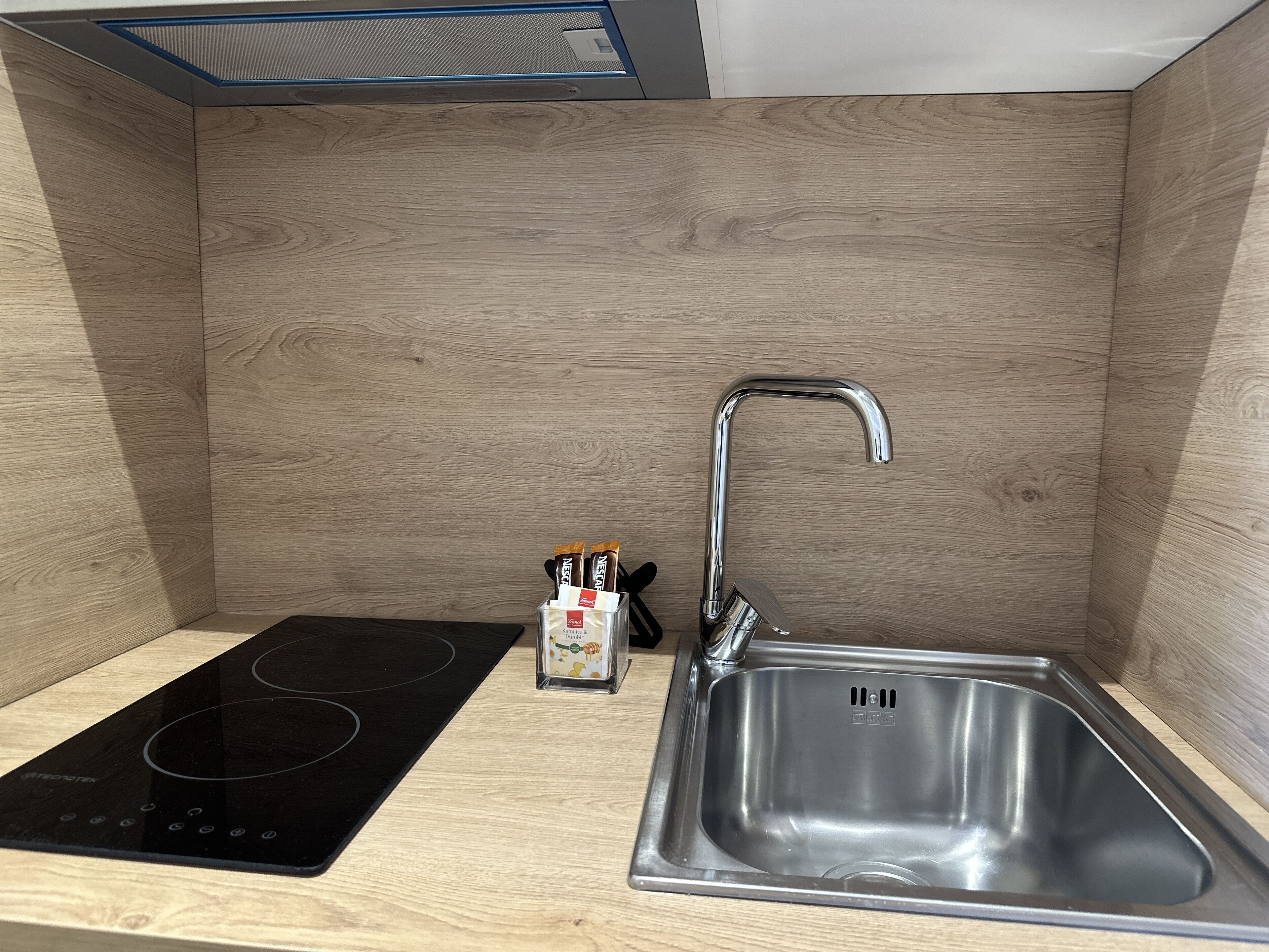 A compact kitchen with a black induction cooktop, a stainless steel sink, and a small cabinet with kitchen utensils.
