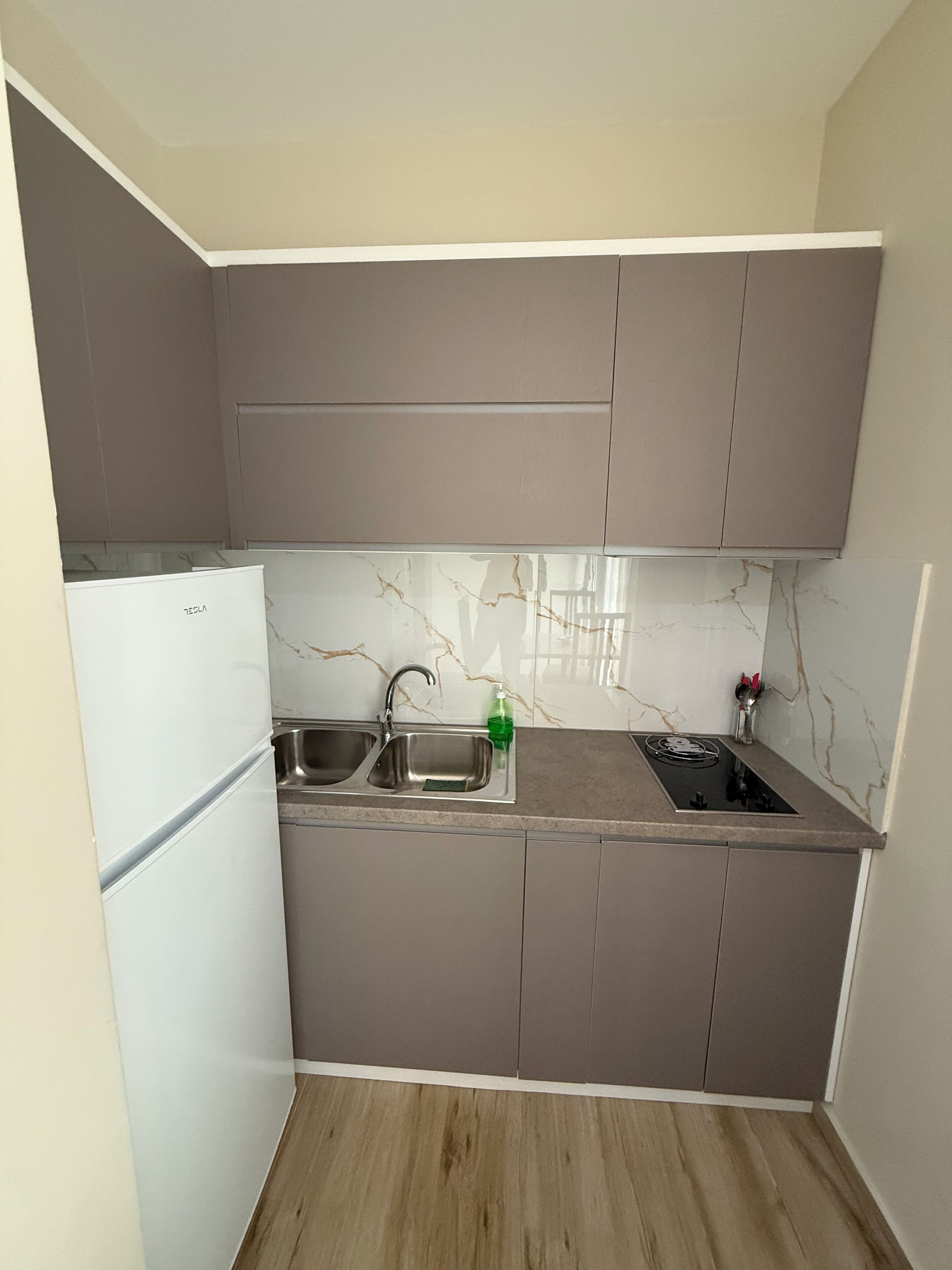 Una cucina compatta con mobili grigi, un frigorifero bianco, un lavello a due vasche e un piano cottura a gas.