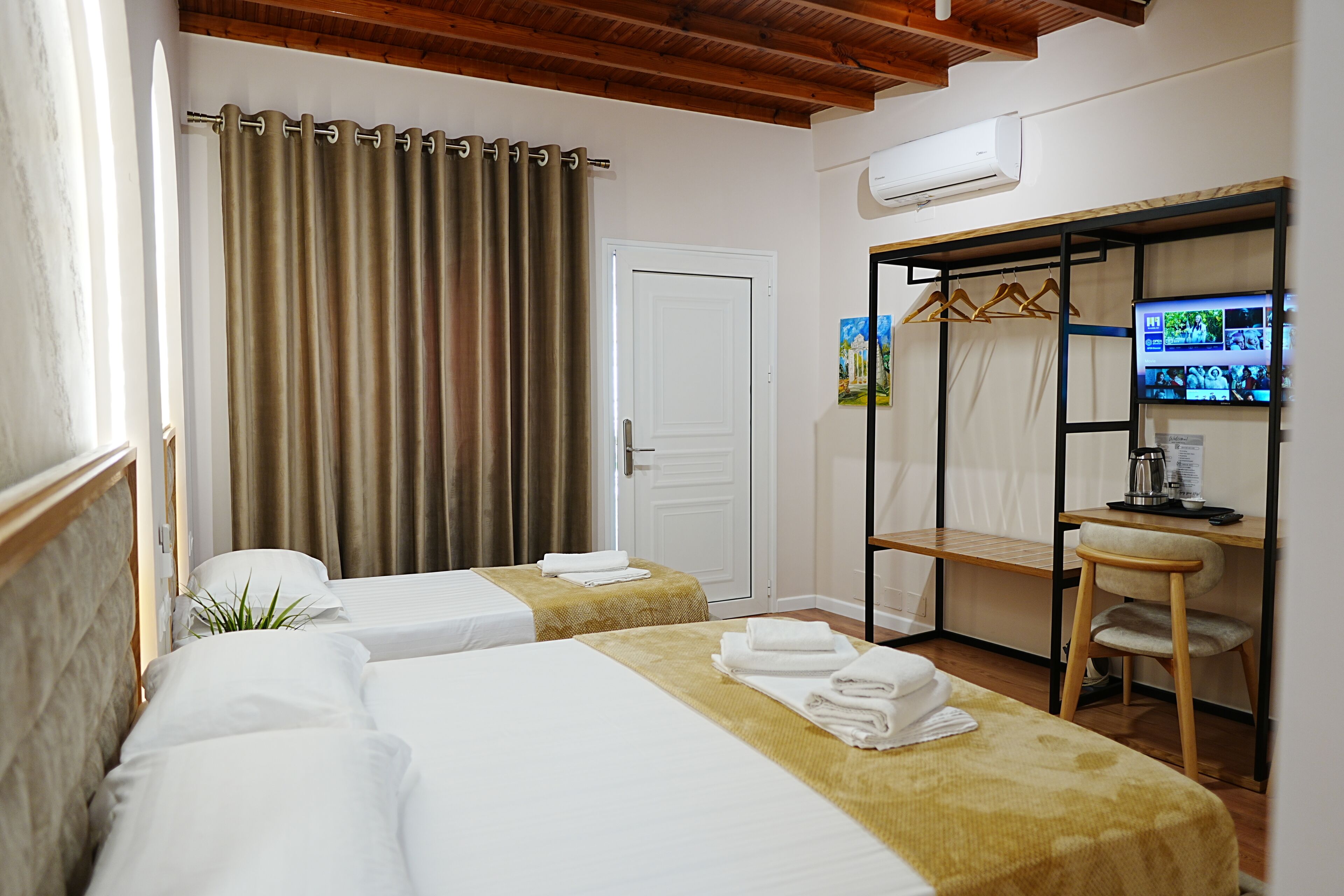 A hotel room with two beds, a desk, a chair, a wardrobe, and a television.