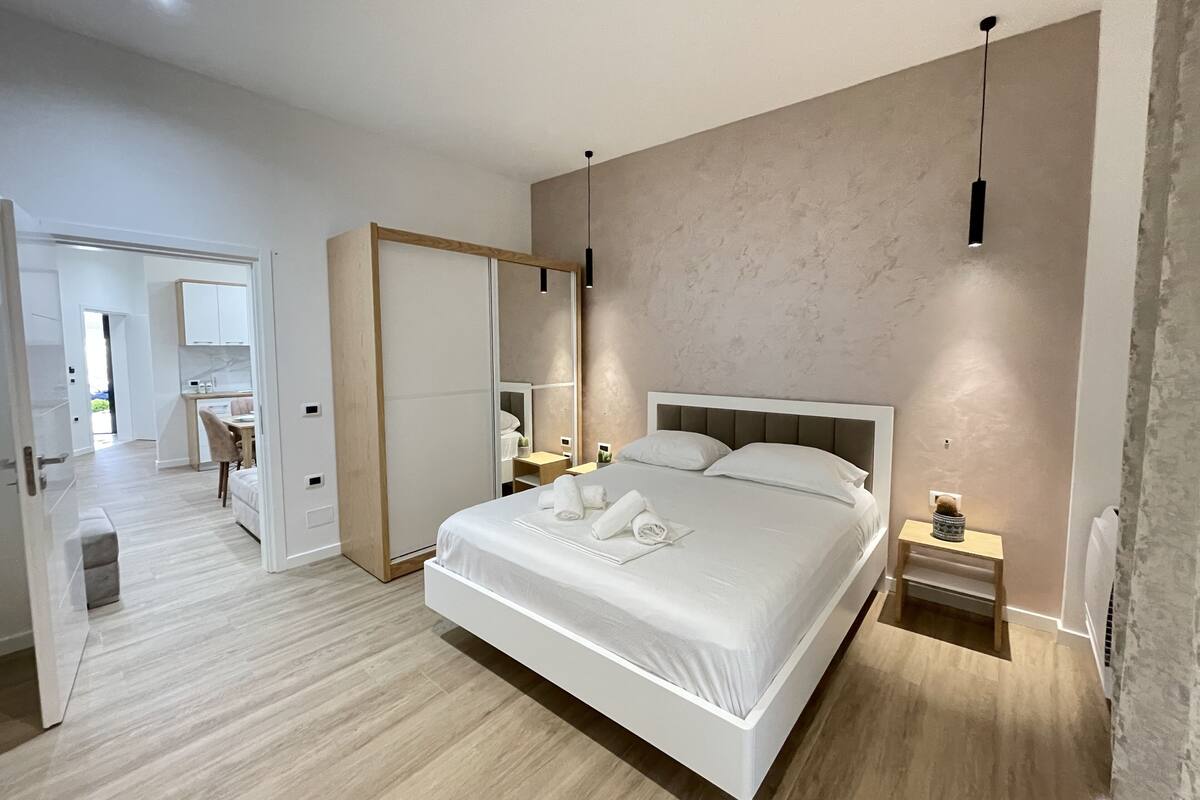 A modern bedroom with a large bed, bedside tables, a wardrobe, and a bathroom visible through an open door.