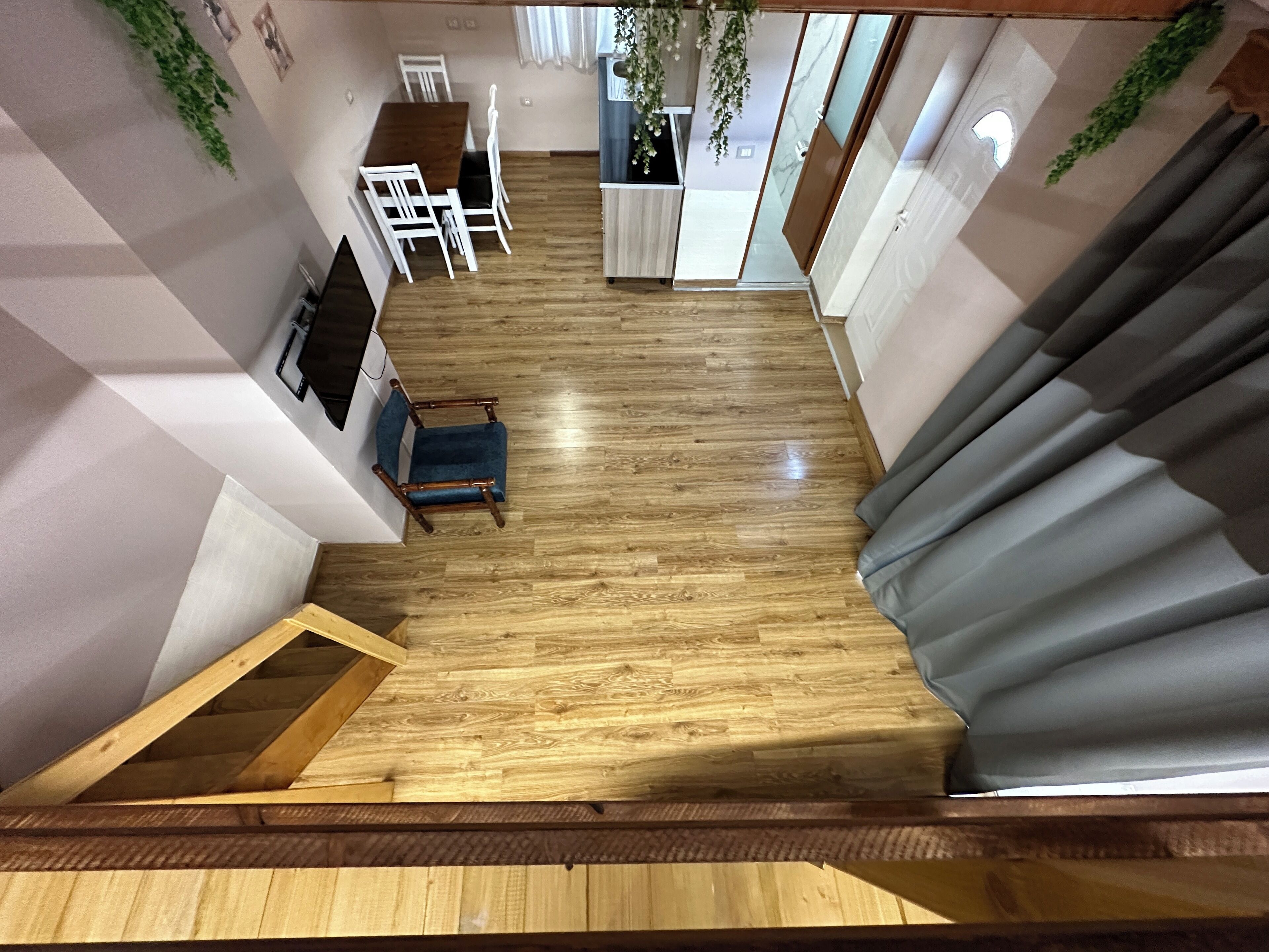 A spacious room with a wooden floor, a blue chair, a dining table with chairs, and a staircase with a wooden railing.