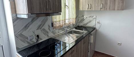 Una cocina con armarios de madera, encimera negra, un lavabo y una ventana con cortina.