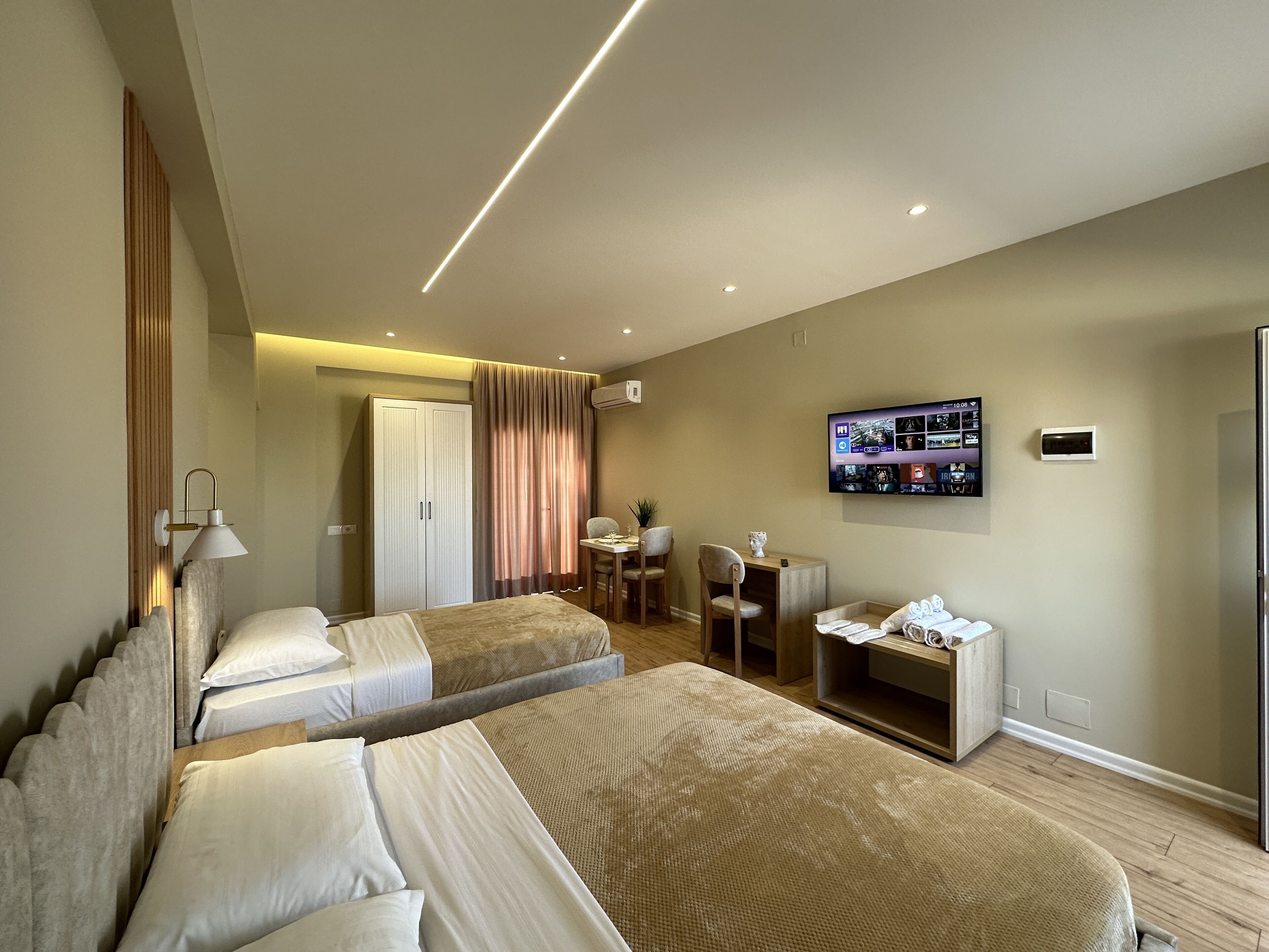 A modern hotel room with two beds, a desk, a chair, a TV, and an air conditioning unit.