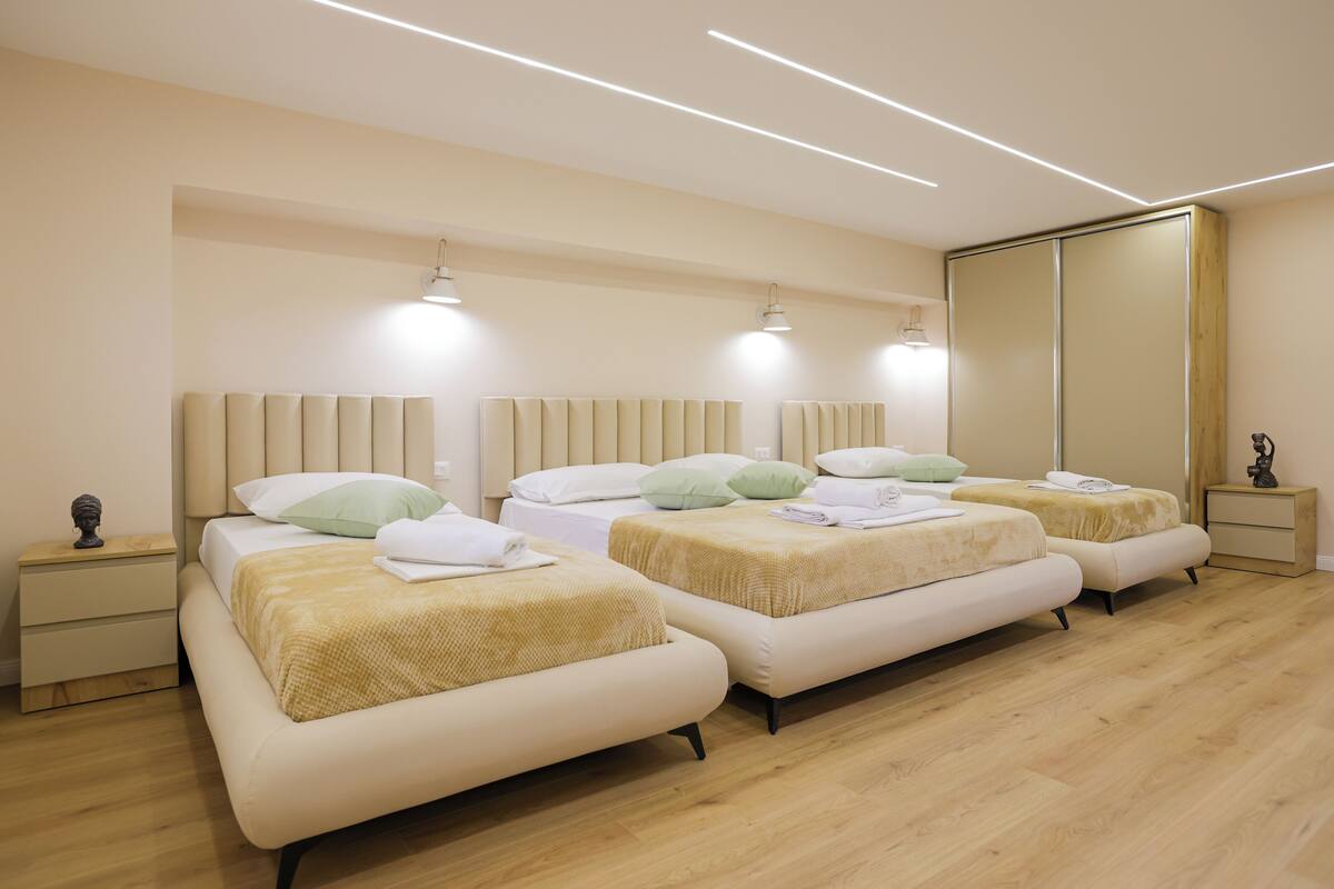 A modern hotel room with three beds, wooden flooring, and a large mirror.