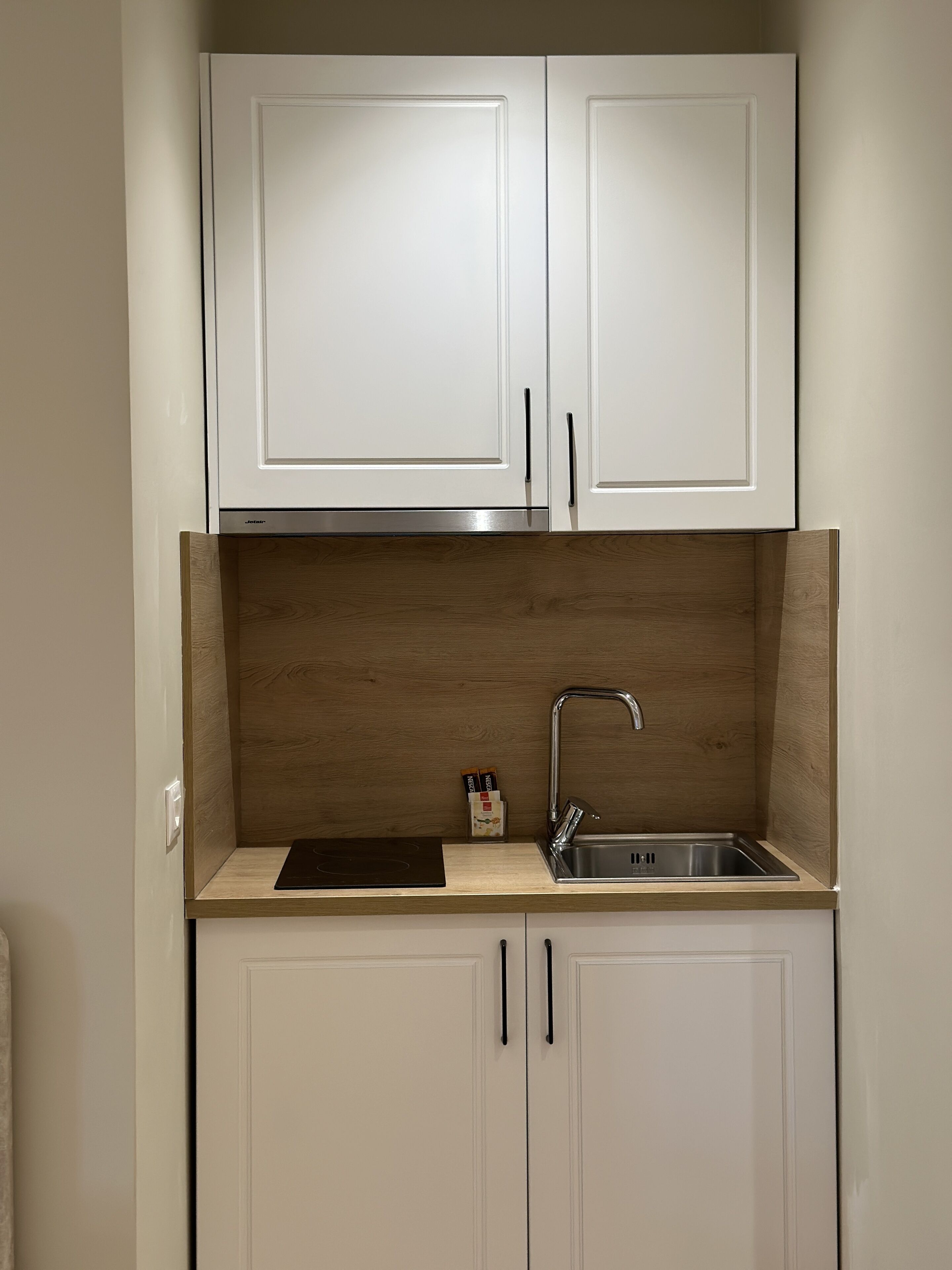 Cocina compacta con armarios blancos, un lavamanos de acero inoxidable y un protector de pared de madera.
